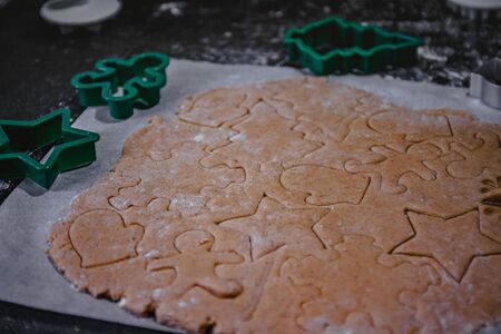 cut out gingerbread cookie in the form of a Christmas tree, star, little man, hearts from raw dough on parchment baking paper on a dark background. Top view. save space.の写真素材