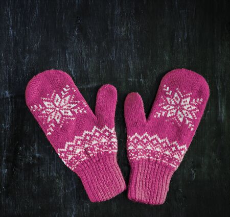 a pair of red-pink-lilac-magenta purple knitted mittens on a dark blue-green-brown wooden vintage background, copy space.の写真素材
