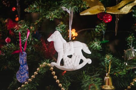 Christmas toys in the form of a white ceramic antique rocking horse with gifts on a decorated Christmas tree. Close-upの写真素材