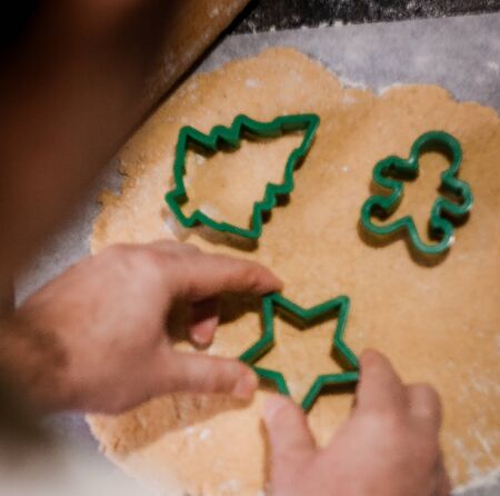 male hands cut out gingerbread cookie in the form of a snowflake, Christmas tree, a man from raw dough on parchment baking paper on a dark background. View from above. save space.の写真素材
