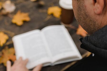 male female reads a book in autumn park drinks takeaway coffee coffee. Close-up over shoulder, blurred. top view, save space. Seen hands. In a dark retro style.の写真素材