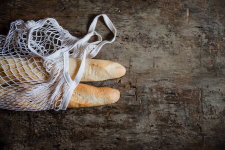 Fresh rosy baguettes in a string bag on a dark wooden retro background. Top view, copy space.の写真素材