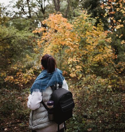 Hiking woman at autumn forest. Backpacker standing in woodland during fall season. Enjoying hike in nature at sunny day.の写真素材