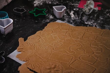 cut out gingerbread cookie in the form of a Christmas tree, star, little man, hearts from raw dough on parchment baking paper on a dark background. Top view. save space.の写真素材