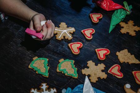 decorate Christmas gingerbread cookies using colored glaze on a dark wooden table, top view.の写真素材