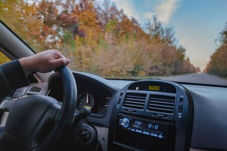 A man driving a car on an autumn yellow-orange road. Close-up of a hand.の写真素材