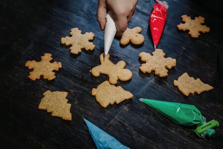 decorate Christmas gingerbread cookies using colored glaze on a dark wooden table, top view.の写真素材