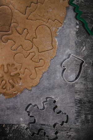 cut out gingerbread cookie in the form of a Christmas tree, star, little man, hearts from raw dough on parchment baking paper on a dark background. Top view. save space.の写真素材
