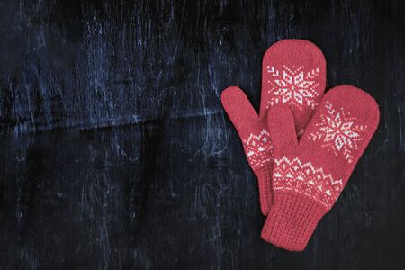 a pair of red-pink-lilac-magenta purple knitted mittens on a dark blue-green-brown wooden vintage background, copy space.の写真素材