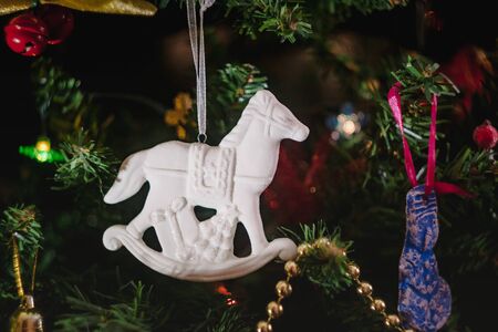 Christmas toys in the form of a white ceramic antique rocking horse with gifts on a decorated Christmas tree. Close-upの写真素材