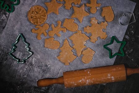 cut out gingerbread cookie in the form of a Christmas tree, star, little man, hearts from raw dough on parchment baking paper on a dark background. Top view. save space.の写真素材