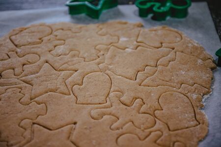 cut out gingerbread cookie in the form of a Christmas tree, star, little man, hearts from raw dough on parchment baking paper on a dark background. Top view. save space.の写真素材