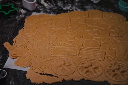 cut out gingerbread cookie in the form of a Christmas tree, star, little man, hearts from raw dough on parchment baking paper on a dark background. Top view. save space.の写真素材