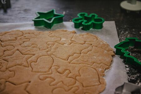 cut out gingerbread cookie in the form of a Christmas tree, star, little man, hearts from raw dough on parchment baking paper on a dark background. Top view. save space.の写真素材