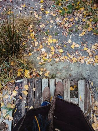 top view of female legs with brown boots on a background of yellow autumn leaves and a wooden platform. Copy spaceの写真素材