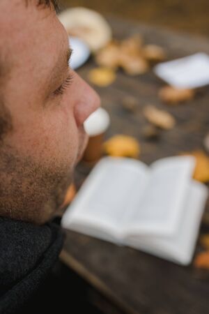 male female reads a book in autumn park drinks takeaway coffee coffee. Close-up over shoulder, blurred. top view, save space. Seen hands. In a dark retro style.の写真素材