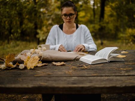 male female reads a book in autumn park drinks takeaway coffee coffee. Close-up over shoulder, blurred. top view, save space. Seen hands. In a dark retro style.の写真素材