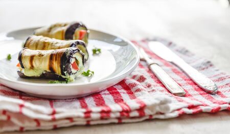 traditional dish three rolls of fried eggplant, cottage cheese and tomato on a white plate on a light background. Minimalism. View from above.の写真素材