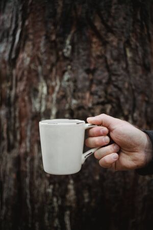 hand holds a cup of tea with coffee on the background of an old wooden trunk. Warm autumn atmosphere, soft focusの写真素材