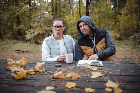 Handsome loving couple sitting on the bench in the autumn park reading a book, having fun together. Love and tenderness. Relationships, friendships, education, lifestyle concept.の写真素材