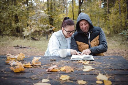 Handsome loving couple sitting on the bench in the autumn park reading a book, having fun together. Love and tenderness. Relationships, friendships, education, lifestyle concept.の写真素材