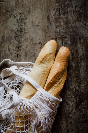 Fresh rosy baguettes in a string bag on a dark wooden retro background. Top view, copy space.の写真素材