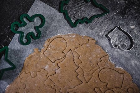 cut out gingerbread cookie in the form of a Christmas tree, star, little man, hearts from raw dough on parchment baking paper on a dark background. Top view. save space.の写真素材