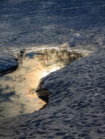 Landscape reflection of the setting sun in the ice hole on a snowy ice lake.の写真素材