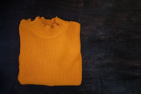 Folded yellow knitted sweater on a dark wooden background with copy space. Flat lay.の写真素材