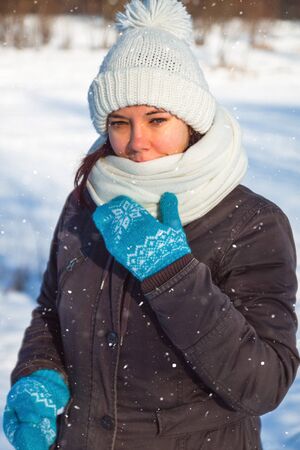 Happy young european woman in white knitted hat and scarf and blue holiday mittens laughing under the snow.の写真素材