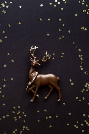 Miniature deer on a dark background with shiny stars with copy space. Christmas composition, postcard template. Flat lay.の写真素材