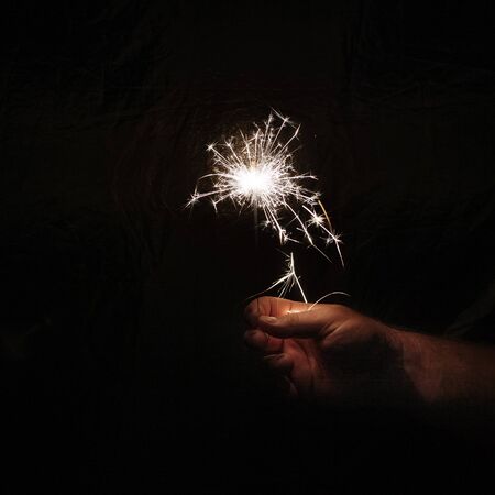 Hand with sparkler on dark background. Celebrating new year with sparkler. Hand holding sparkler on dark background. Christmas fun. New year concept.の写真素材