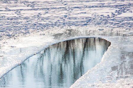Landscape reflection of trees in a forest in an ice hole on a snowy ice lake.の写真素材
