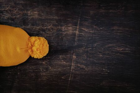 Knitted yellow hat with balabon on a dark wooden background with copy space. View from above.の写真素材