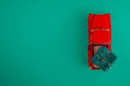 a miniature red car in the back carries a gift on a simple green-aquamarine background, top view. Save the space. Concept, festive Christmas mood, gift delivery. The trendの写真素材