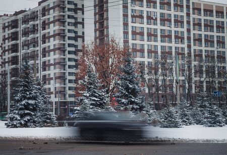 a car in motion rides along a tall building on a winter road in snowの写真素材