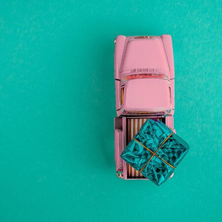 a miniature pink car in the back carries a gift on a simple blue-aquamarine background, top view. Save the space. Concept, festive Christmas mood, gift delivery. The trendの写真素材