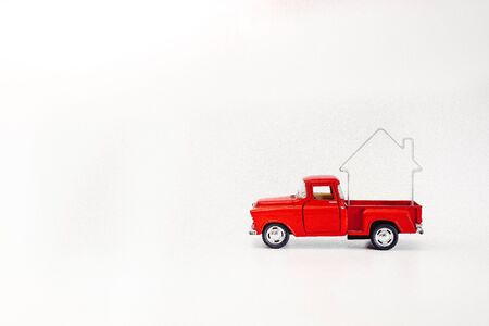 miniature red retro car pickup driven by a house isolated on a white background.の写真素材