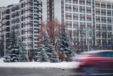 a car in motion rides along a tall building on a winter road in snow.の写真素材