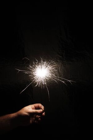 Hand with sparkler on dark background. Celebrating new year with sparkler. Hand holding sparkler on dark background. Christmas fun. New year concept.の写真素材