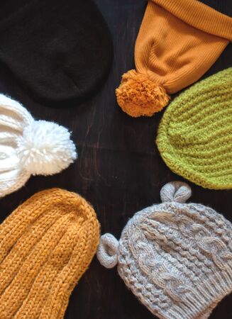 Different types of knitted hats yellow, green, white, gray on a dark wooden background with copy space. View from above.の写真素材