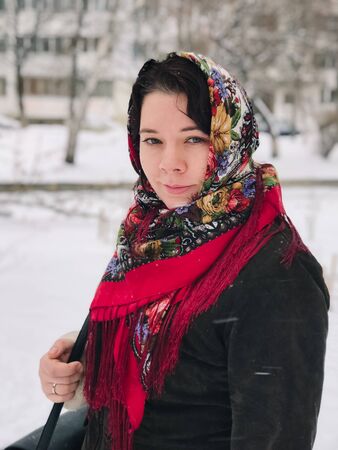 Portrait of a young caucasian happy woman in national russian patterned shawl on a snowy winter dayの写真素材
