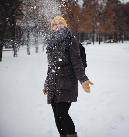Happy young european woman in a yellow knitted hat and mittens with a backpack, laughs under the snowfall. Retro effect. Blurの写真素材