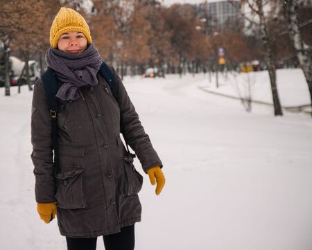 Happy young european woman in a yellow knitted hat and mittens with a backpack, laughs under the snowfall. Retro effect. Blurの写真素材