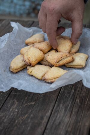 Man's hand takes curd shortbread cookies with triangles on white parchment on an old dark wooden background.の写真素材