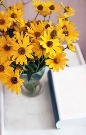 A vase of yellow daisy flowers on a table next to a thick book. Minimalism Life style, naturalness. Copy spaceの写真素材