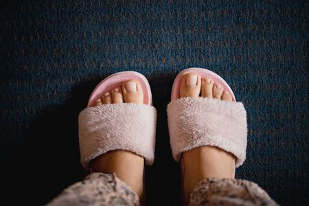 female legs with a pedicure in pink fluffy slippers on a dark blue carpet background. Copy space, flat lay, minimalism.の写真素材