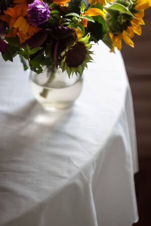 A bouquet with rustic summer wildflowers, sunflowers is on the table with a white tablecloth. Life style. Copy space. Film tinting. moody photo.の写真素材
