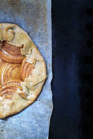 Apple galette - pie on baking parchment and dark background. Copy space, flat lay.の写真素材