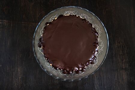 Chocolate round cake on a glass stand on a dark wooden background. Flat lay, minimalism, symmetry. Copy spaceの写真素材